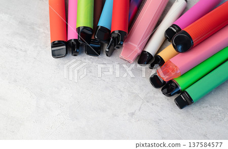 Collection of various colorful disposable e-cigarettes and vape pens scattered on a light grey background. 137584577
