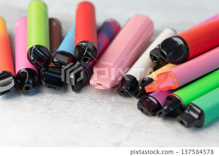 Collection of various colorful disposable e-cigarettes and vape pens scattered on a light grey background. 137584578