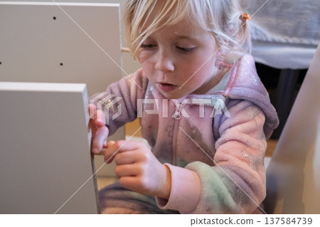 Independent 4 year old girl assembling furniture with a screwdriver in a modern home interior 137584739