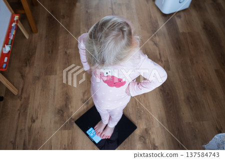 Cute 4 year old Caucasian girl standing on weighing scales Cute 4 year old Caucasian girl standing on weighing scales 137584743
