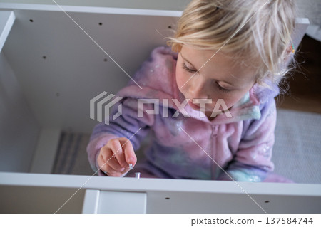 Independent 4 year old girl assembling furniture with a screwdriver in a modern home interior Independent 4 year old girl assembling furniture with a screwdriver in a modern home interior 137584744
