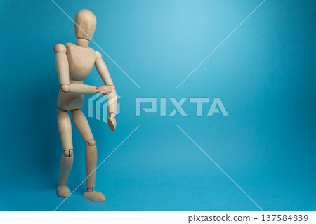 Wooden mannequin posing against a blue background showcasing a bending motion during a dynamic art demonstration Wooden mannequin posing against a blue background showcasing a bending motion during a dynamic art demonstration 137584839