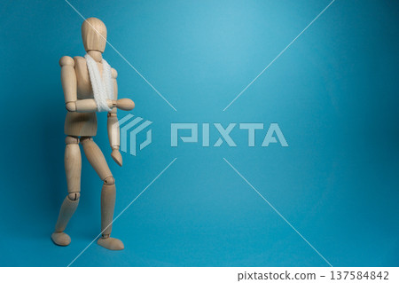 Wooden mannequin holds up an arm in front of blue background while wearing a scarf and facing slightly to the side Wooden mannequin holds up an arm in front of blue background while wearing a scarf and facing slightly to the side 137584842