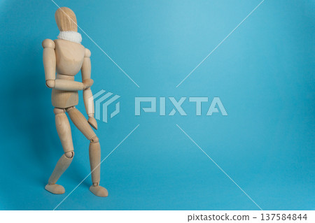 Wooden figure stands against a blue background while holding its arm in a specific pose during a creative art session Wooden figure stands against a blue background while holding its arm in a specific pose during a creative art session 137584844