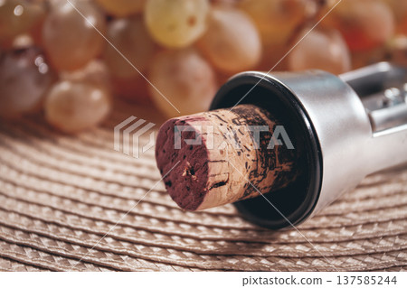 A corkscrew with a wine bottle stopper, lying on a woven napkin, with green grapes, 137585244