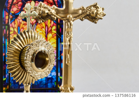 Golden monstrance and crucifix against stained glass background 137586116
