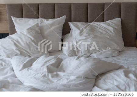 Unmade hotel bed with white pillows and rumpled duvet on mattress in modern bedroom interior. Hospitality concepts, hotel accommodation marketing, travel stay comfort, tourism lodging promotion 137586166