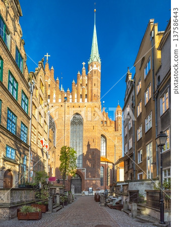 Gdansk, a city on the Baltic coast of northern Poland, Europe. Majestic cathedral towering over a charming cobblestone street, its spire reaching into the clear blue sky in an old European city. Gdansk, a city on the Baltic coast of northern Poland, Europe. Majestic cathedral towering over a charming cobblestone street, its spire reaching into the clear blue sky in an old European city. 137586443