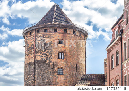 Gdansk, a city on the Baltic coast of northern Poland, Europe. Historic brick tower stands tall against a bright, cloudy sky, showcasing architectural details of a building from a bygone era. 137586446