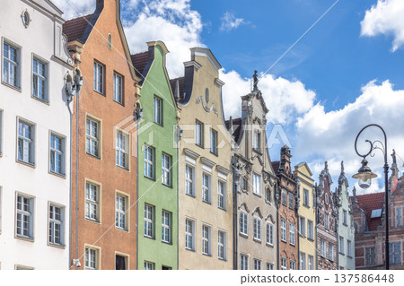 Gdansk, a city on the Baltic coast of northern Poland, Europe. Colorful historic buildings line the street, each with unique architectural details and hues against a bright blue sky with fluffy clouds 137586448
