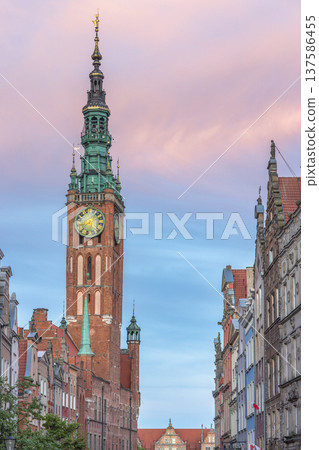 Gdansk, a city on the Baltic coast of northern Poland, Europe. Majestic tower clock dominates historical cityscape against pink-tinged sky, showcasing architectural grandeur and timeless elegance. 137586455