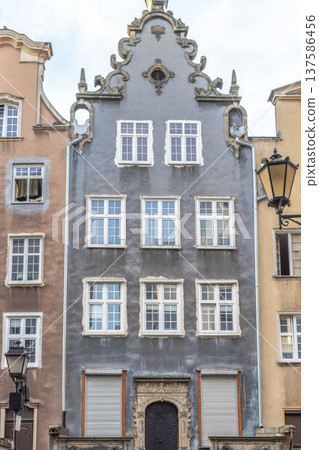 Gdansk, a city on the Baltic coast of northern Poland, Europe. Architectural facade of a tall building with gray walls and several white-framed windows, showcasing old-world charm and intricate design 137586456