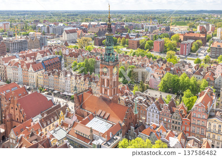 Gdansk, a city on the Baltic coast of northern Poland, Europe. Aerial view of an old European city featuring a prominent church tower with clock faces surrounded by colorful buildings and green trees. 137586482