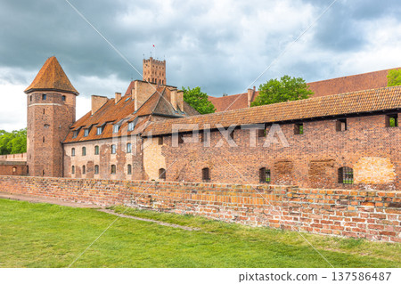 The Malbork Castle, a brick Gothic castle in northern Poland, Europe. Majestic medieval castle with red brick walls, towers, and tiled roofs, standing tall against a cloudy sky in a historic landscape 137586487