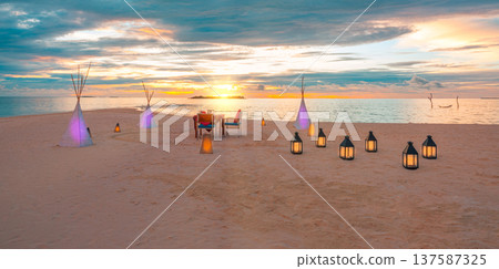 Serene tropical beach wedding at golden sunset with vibrant candles and floral arch over pristine ocean idyllic colorful sky romantic honeymoon anniversary getaway 137587325