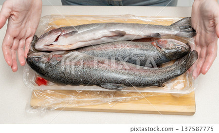 Freshly caught whole fish displayed on a wooden cutting board, hands positioned to showcase the fish in a kitchen setting 137587775