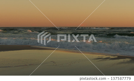 Sunset illuminating ocean waves, creating a serene atmosphere with reflections on wet sand and gentle surf sounds 137587779
