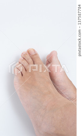Close-up view of two bare feet resting on a clean white surface, showcasing natural skin texture and relaxed positioning in a serene environment Close-up view of two bare feet resting on a clean white surface, showcasing natural skin texture and relaxed positioning in a serene environment 137587784