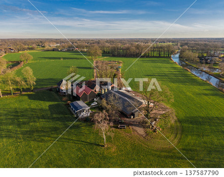 Aerial view of a traditional European farmstead surrounded by vibrant green pastures and a winding river. A peaceful rural landscape featuring farm buildings and autumn trees under a blue sky. Aerial view of a traditional European farmstead surrounded by vibrant green pastures and a winding river. A peaceful rural landscape featuring farm buildings and autumn trees under a blue sky. 137587790
