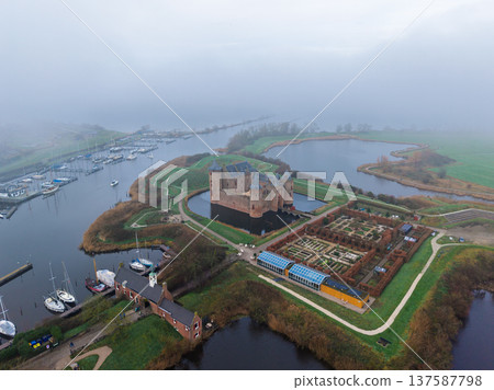 Aerial view of the medieval Muiderslot castle in the Netherlands. Historic fortress with a moat, gardens, and harbor under a misty sky. Famous Dutch landmark and tourist attraction. Aerial view of the medieval Muiderslot castle in the Netherlands. Historic fortress with a moat, gardens, and harbor under a misty sky. Famous Dutch landmark and tourist attraction. 137587798