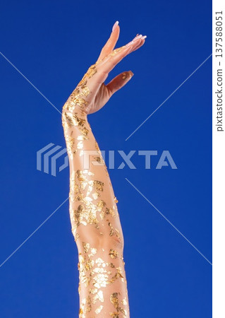 Arm raised covered in golden flakes against bright blue backdrop displaying elegance and beauty Arm raised covered in golden flakes against bright blue backdrop displaying elegance and beauty 137588051