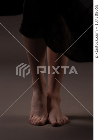 Woman in dark dress stands barefoot on plain surface, showing only legs and feet 137588059
