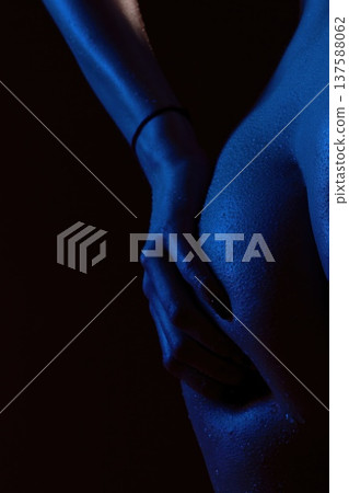 Woman holds her shoulder in studio with blue lighting and black background 137588062