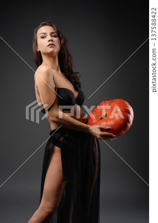 Beautiful woman poses with a pumpkin under dramatic lighting Beautiful woman poses with a pumpkin under dramatic lighting 137588422