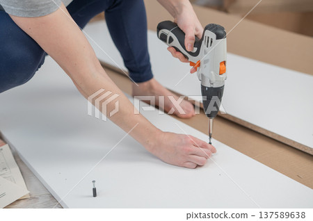 A Caucasian woman uses a screwdriver to tighten a screw while assembling a cabinet. A Caucasian woman uses a screwdriver to tighten a screw while assembling a cabinet. 137589638