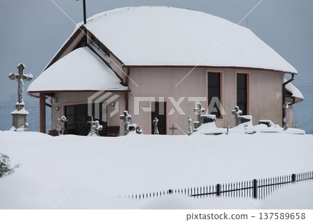 Snow-covered chapel beside a small cemetery with stone crosses in winter. Snow-covered chapel beside a small cemetery with stone crosses in winter. 137589658