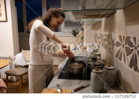 Young woman cooking dinner seasoning food in kitchen 137589753