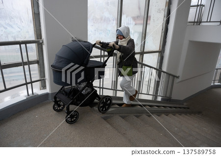 Young mother pushing stroller up residential building stairs Young mother pushing stroller up residential building stairs 137589758