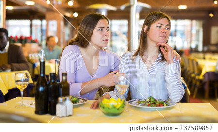 Woman calming upset female friend in restaurant during dinner Woman calming upset female friend in restaurant during dinner 137589852