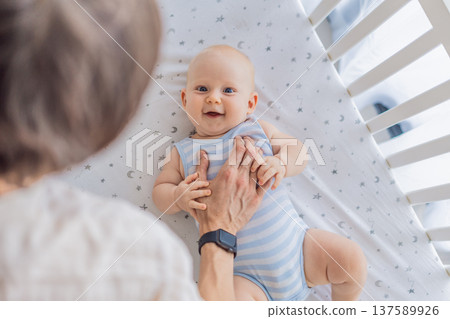 Father gently placing his baby into a crib at home, creating a calm and safe bedtime moment. Caring fatherhood scene filled with trust and warmth. Parenting, infant sleep and family bonding concept Father gently placing his baby into a crib at home, creating a calm and safe bedtime moment. Caring fatherhood scene filled with trust and warmth. Parenting, infant sleep and family bonding concept 137589926