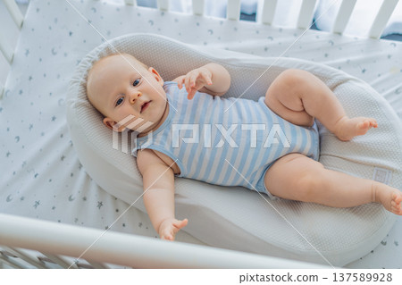 Baby lying peacefully in a cozy cocoon nest inside a crib, feeling safe and calm at home. Soft light and warm atmosphere highlight comfort and care. Infant sleep, safety and gentle parenting concept Baby lying peacefully in a cozy cocoon nest inside a crib, feeling safe and calm at home. Soft light and warm atmosphere highlight comfort and care. Infant sleep, safety and gentle parenting concept 137589928