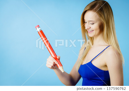 Positive woman holds big pencil in hand Positive woman holds big pencil in hand 137590762