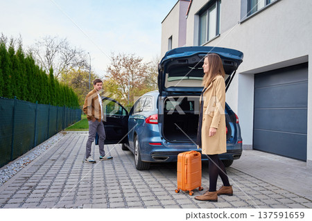 Man and woman standing near car with open trunk and suitcase outside building Man and woman standing near car with open trunk and suitcase outside building 137591659