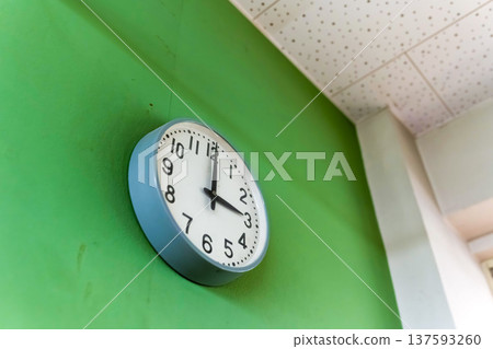 一面綠色的牆上掛著一個類比時鐘 137593260
