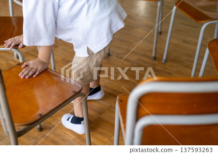 Elementary school boy arranging chairs in classroom Elementary school boy arranging chairs in classroom 137593263