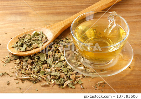 A glass cup of lemon balm tea, surrounded by dried leaves in a bowl, and a wooden spoon 137593606