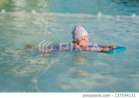 preschool child girl learning to swim with board in swimming pool 137594131