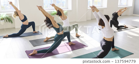 Synchronized yoga practitioners arching in crescent lunge sequence across studio Synchronized yoga practitioners arching in crescent lunge sequence across studio 137594779