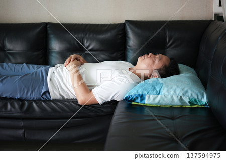 A man takes a peaceful nap on the sofa during the day. The quiet atmosphere reflects comfort, rest, and relaxation at home. 137594975