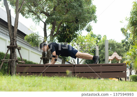 A man performs an incline push-up on a park bench, focusing on strengthening chest, shoulders, and triceps while improving upper body endurance. 137594993