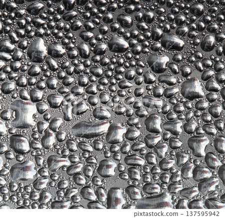 Macro view of water droplets and condensation forming a textured moisture pattern on a reflective metallic or glass surface, creating an abstract background with natural liquid shapes. 137595942