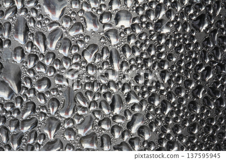Macro view of water droplets and condensation forming a textured moisture pattern on a reflective metallic or glass surface, creating an abstract background with natural liquid shapes. Macro view of water droplets and condensation forming a textured moisture pattern on a reflective metallic or glass surface, creating an abstract background with natural liquid shapes. 137595945