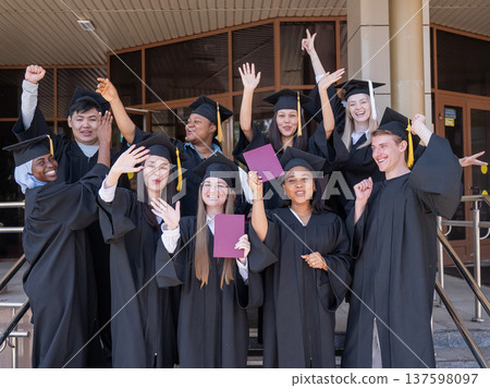 Happy students of different nationalities in graduation gowns hold their diplomas. Happy students of different nationalities in graduation gowns hold their diplomas. 137598097