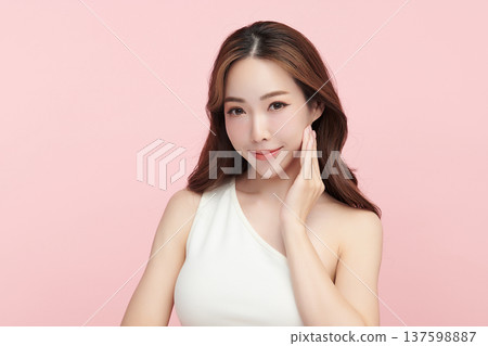 A beautiful young Asian woman with clean, fresh skin against a pink background. Skincare, facial treatment, cosmetology, beauty, and spa. An elegant portrait of an Asian woman. 137598887