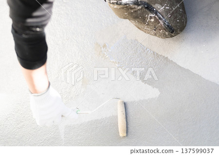 Balcony waterproofing maintenance: Worker applying waterproofing material with a long-handled roller Balcony waterproofing maintenance: Worker applying waterproofing material with a long-handled roller 137599037