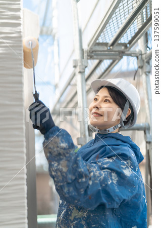 一位女工匠正在外牆粉刷工地工作:施工現場,她微笑著用滾筒塗刷油漆。 一位女工匠正在外牆粉刷工地工作:施工現場,她微笑著用滾筒塗刷油漆。 137599051